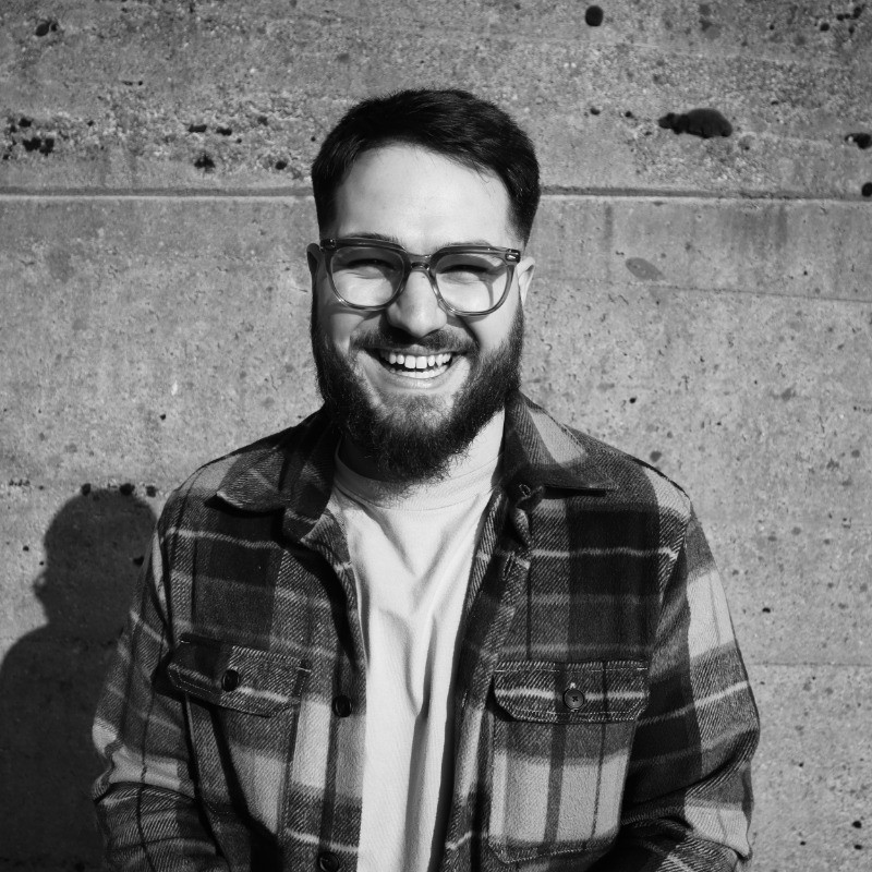 Un homme barbu à lunettes qui fait un grand sourire à la camera