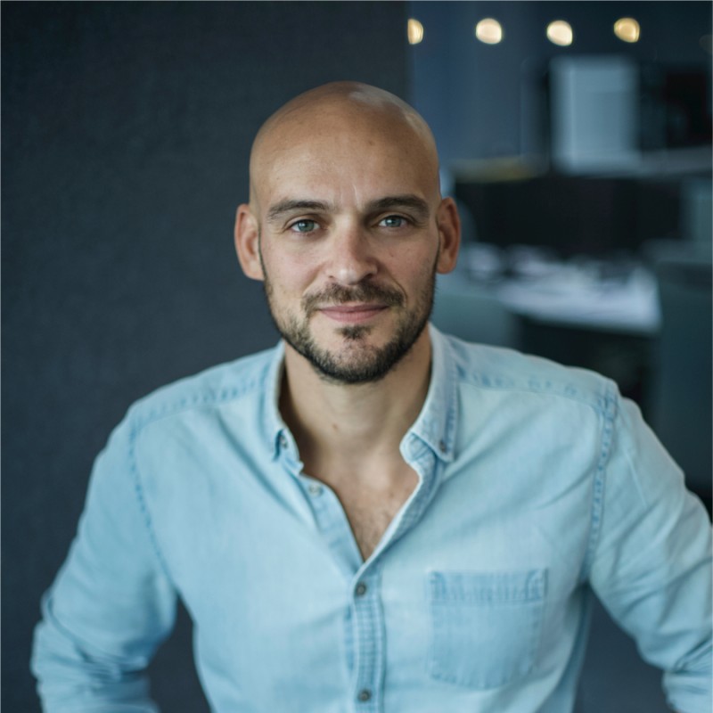 Un homme en chemise et aux yeux bleu ciel sourit à la caméra